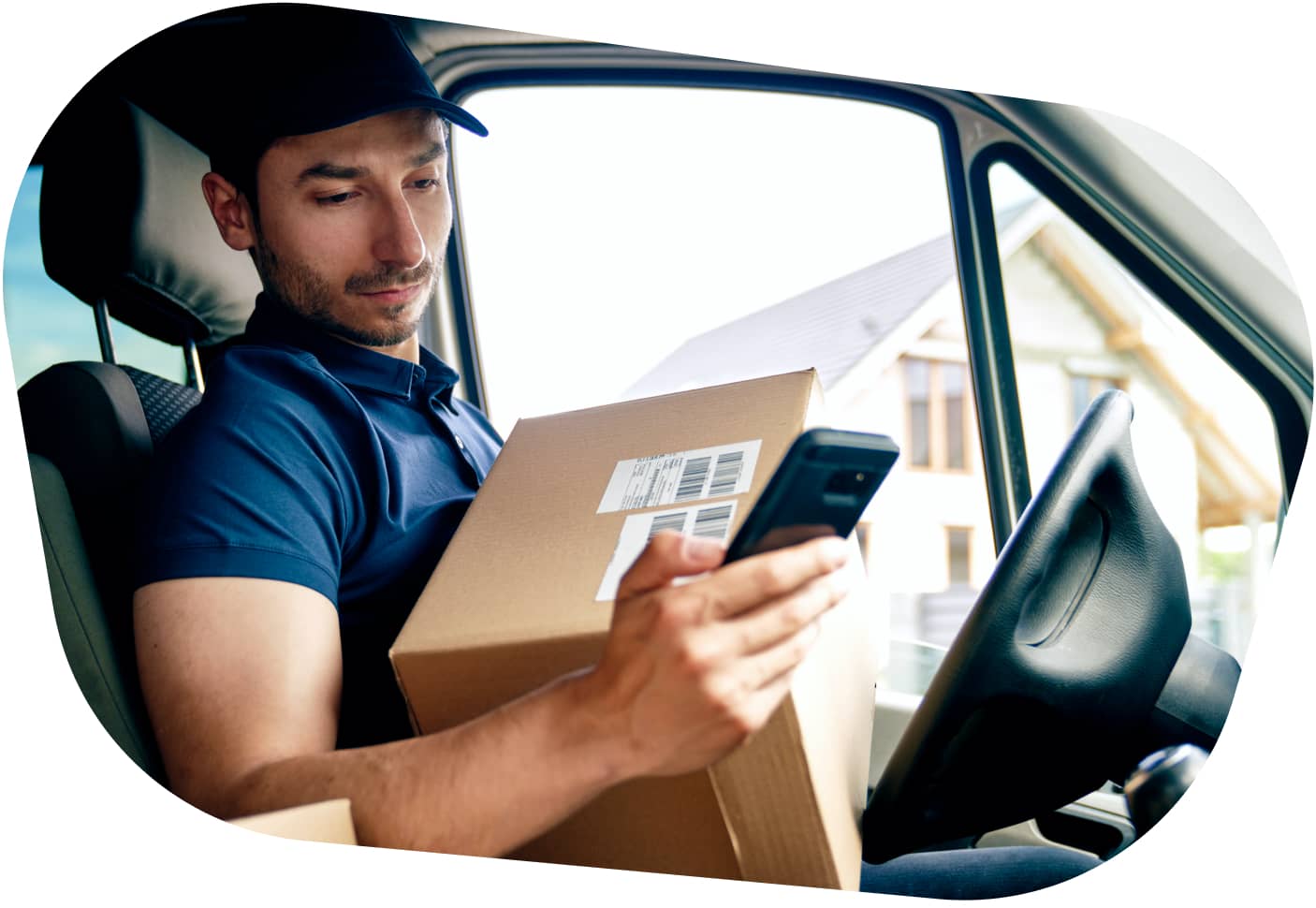 A carGO Health driver sitting in a vehicle, holding a package on his lap while checking his phone.