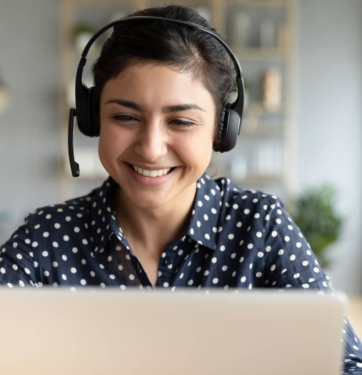 A smiling customer support representative wearing a headset, looking at a laptop screen.